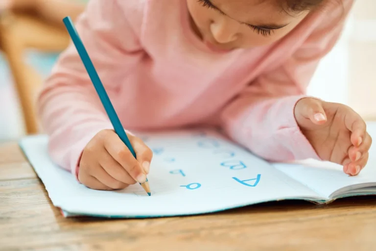 Young child in a pink jumper practising handwriting with a blue pencil