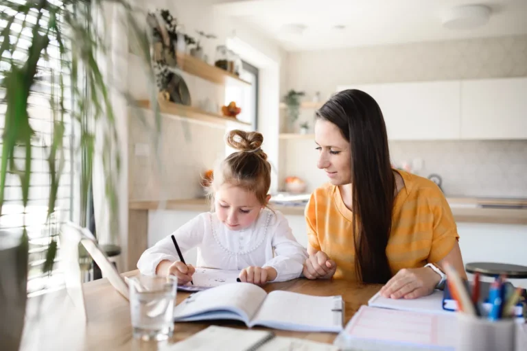 Mum in a yellow top working through homework with her daughter at the kitchen table