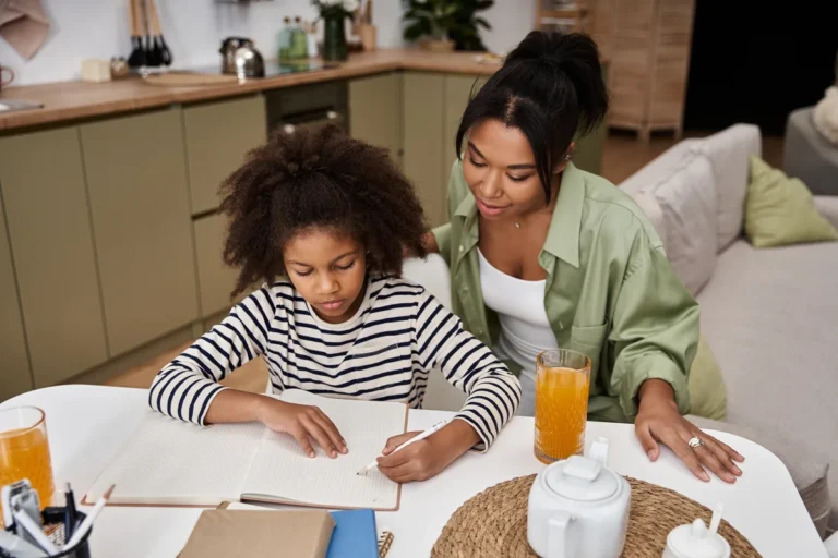 Mum sitting beside her daughter at the kitchen table helping with homework