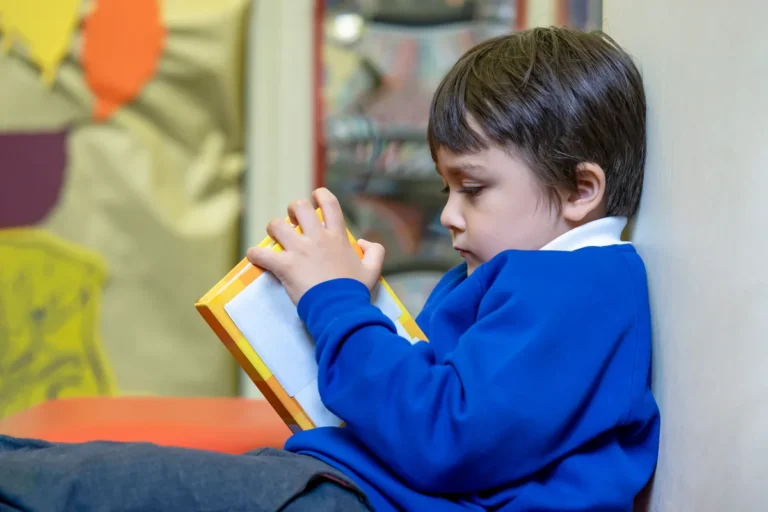 Primary school boy in a blue school jumper reading a book in class