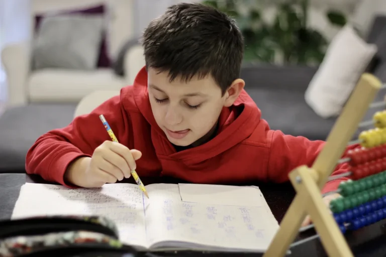 Boy in a red hoodie practising maths in his exercise book with an abacus beside him